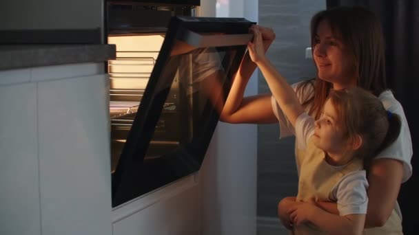 The family cooks together. Mother and daughter put the pie in the oven and close the door. Watch and wait for homemade pizza cooking. Happy childhood, help your mother. — Stock Video