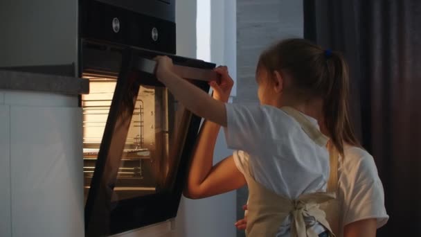 Una niña ayuda a su madre en la cocina y cierra la puerta del horno. Madre asistente preescolar. Niño feliz en la familia — Vídeo de stock