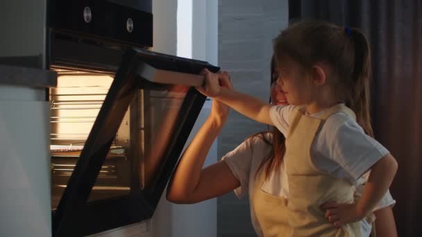 Die Familie kocht zusammen. Mutter und Tochter legen den Kuchen in den Ofen und schließen die Tür. Beobachten und warten Sie auf hausgemachte Pizzakochen. Glückliche Kindheit, hilf deiner Mutter. — Stockvideo