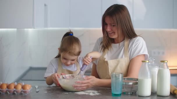 Riendo mamá y su hija están cocinando en la cocina. La niña aprende de su madre cómo hacer un pastel. Feliz infancia. — Vídeos de Stock