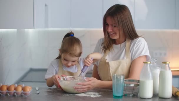 Смеющиеся мама и дочь готовят на кухне. Девочка учится у матери печь пирог. Счастливого детства — стоковое видео