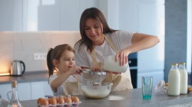 Anne ve kızı mutfakta önlüklerle birlikte yemek pişiriyor, bir kaseye un ekliyor ve kıza nasıl tatlı yapılacağını öğretiyor. Küçük aile şirketi.
