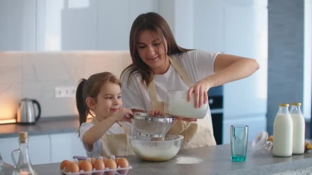 Мама і дочка готують разом в фартухах на кухні, додають борошно до миски і навчають дівчинку робити десерти. Маленький родинний бізнес. — стокове відео