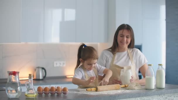 Μητέρα Βοηθώντας Κόρη Roll Dough στην κουζίνα για να ψήσετε τα μπισκότα. Η μαμά και η κόρη ψήνουν πίτσα στην κουζίνα μαζί. Κορίτσι βοηθά τη μαμά της να κυλήσει το χρήμα με ένα πλάστη. — Αρχείο Βίντεο