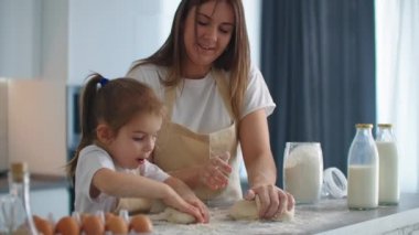 Anne, kızına mutfakta kurabiye için hamur yoğurmayı yavaş çekimde öğretiyor. Anne küçük kızına oklavayla hamur yoğurmayı öğretiyor. Komik kız annesine kurabiye hazırlamasında yardım ediyor..