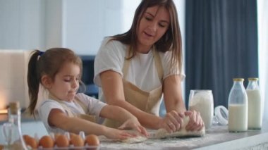 Anne, kızına mutfakta kurabiye için hamur yoğurmayı yavaş çekimde öğretiyor. Anne küçük kızına oklavayla hamur yoğurmayı öğretiyor. Komik kız annesine kurabiye hazırlamasında yardım ediyor..