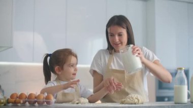 Anne, kızına mutfakta kurabiye için hamur yoğurmayı yavaş çekimde öğretiyor. Anne küçük kızına oklavayla hamur yoğurmayı öğretiyor. Komik kız annesine kurabiye hazırlamasında yardım ediyor..