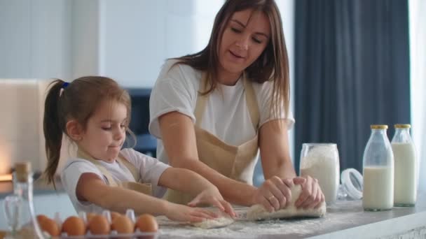 Mother teaching daughter to knead dough for cookies on kitchen in slow motion. Mom teaching kid daughter learning kneading dough with rolling pin, funny child girl helping mother preparing cookies. — Stock Video