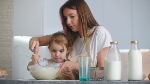 Feliz mamá y sonriente hija mezclar la harina y la leche juntos y batir la masa en un tazón con un batidor — Vídeos de Stock