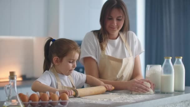 Medium shot van moeder en dochter rollen deeg in de keuken. Mam leert dochter om deeg te koken. Meisje leert gebak bakken. Het deeg samen kneden. Rol het deeg uit voor het bakken. — Stockvideo