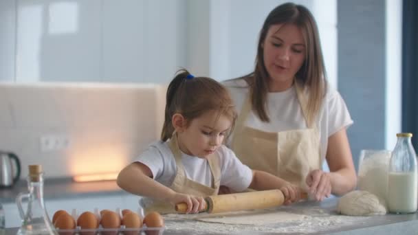 Мама помогает дочери выкачать бабки. Мама з маленькою донькою викидають тісто для печива. за допомогою рулону і печива.. — стокове відео