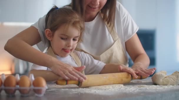 Mittlere Aufnahme von Mutter und Tochter beim Teigrollen in der Küche. Mutter lehrt Tochter Teig kochen. Mädchen lernt Gebäck zu kochen. Den Teig zusammenkneten. Teig zum Backen ausrollen. — Stockvideo