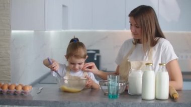Bir anne, küçük kızının mutfakta önlükle yemek yapmayı öğrenmesini izler. Bağımsız kız. Paylaşılan ev izolasyonu