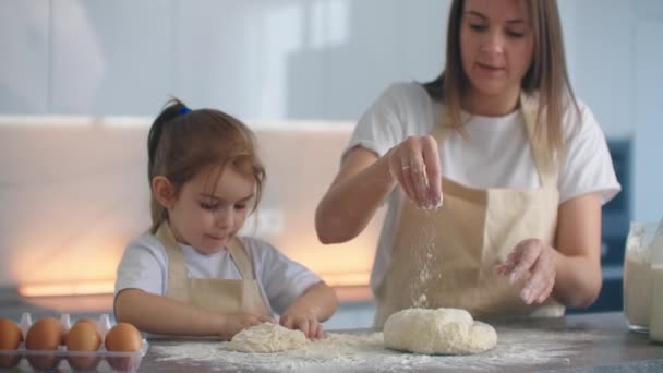 Aprender recetas familiares. Mamá enseña a su hija a hacer un espacio en blanco para la pizza o la torta hecha con las manos de la masa. Las manos mezclan la masa con una hija pequeña . — Vídeos de Stock