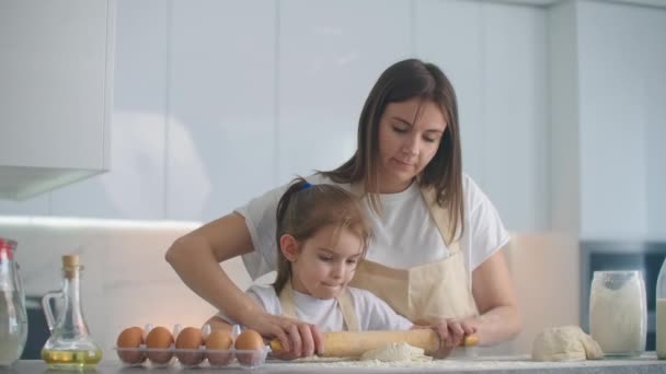 Mom helping daughter to roll out dough. Mom and little daughter roll out the dough for making cookies. using rolling pin and making biscuits. — Stock Video