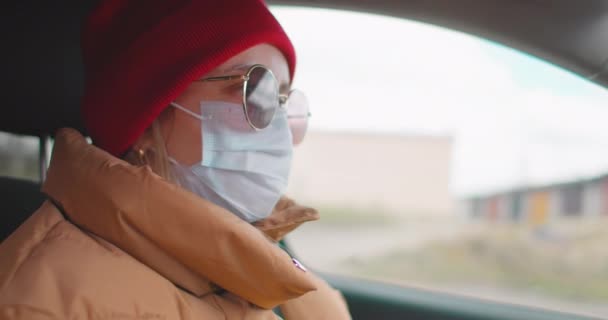 Movimento lento: mulher branca europeia dirigindo um carro e vestindo máscara facial cirúrgica branca como forma de proteção contra coronavírus e gripe . — Vídeo de Stock