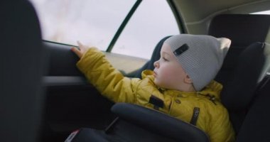 Ağır çekim: Sarı ceketli, hayalperest genç bir çocuk arabanın arka koltuğunda oturur ve pencereden gülümseyerek dışarı bakar. 2 yıllık hayalperest bir çocuk. Küçük gezginin yüz ifadeleri..
