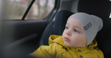 Arabayla seyahat eden küçük çocuk. 2 yaşında beyaz bir çocuk arabanın camından dışarı bakıyor. İki yaşında beyaz bir çocuk, emniyet kemeri takıyor. Arabasında oturuyor ve hareket halindeki bir aracın camından dışarı bakıyor..