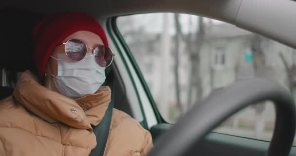 Λευκή γυναίκα φοράει μάσκα προσώπου ενώ οδηγεί κατά τη διάρκεια της ακραίας επιδημίας του κορωναϊού. Γυναίκα φορώντας προστατευτική μάσκα οδηγεί γύρω από την πόλη κατά τη διάρκεια της πανδημίας COVID19 — Αρχείο Βίντεο