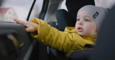 Çocuk arabanın camına bakıyor. Aileyle bir gezi. Pencereden dışarı bakan bebek araba sürüşü seyahatleri. Minik, sevimli bir çocuğun araba koltuğunda oturup pencereden dışarı baktığı orta boy bir fotoğraf.