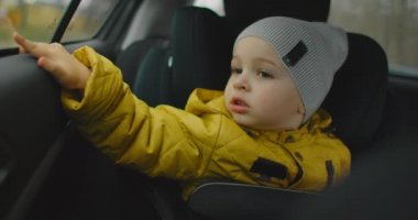 Çocuk arabanın camına bakıyor. Aileyle bir gezi. Pencereden dışarı bakan bebek araba sürüşü seyahatleri. Minik, sevimli bir çocuğun araba koltuğunda oturup pencereden dışarı baktığı orta boy bir fotoğraf.