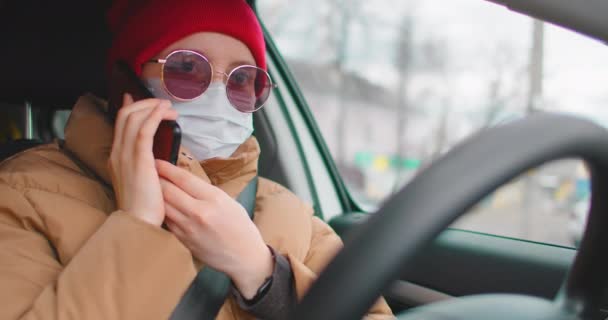 Cámara lenta: Mujer joven con mascarilla protectora estéril en un coche y hablando en un teléfono móvil. Llama al servicio de rescate, concepto de coronavirus pandémico . — Vídeos de Stock