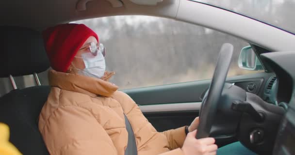 Blanke vrouw draagt gezichtsmasker tijdens het rijden tijdens de extreme coronavirus uitbraak. Vrouw met een beschermend masker rijdt door de stad tijdens de COVID19 pandemie — Stockvideo