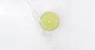 Beyaz arka planda dilimlenmiş limon dilimleri üzerine su püskürtülmüş. Ağır çekimde sulu taze limon