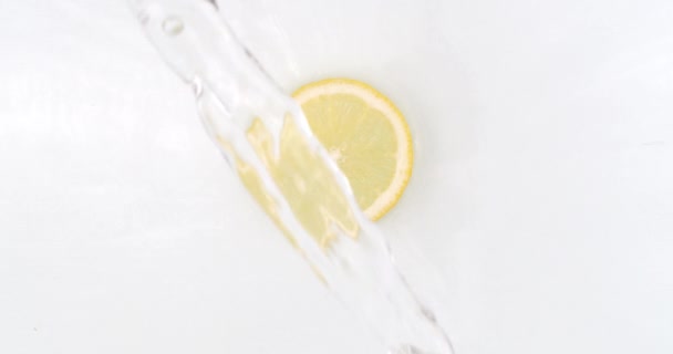 On a white background, a splash of water falls on a slice of lemon in slow motion — Stock Video