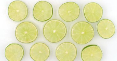Beyaz arka planda dilimlenmiş kireç parçalarına su serpilmiş. Ağır çekimde sulu taze limon. Bir sürü limon dilimi.
