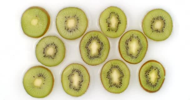 Sobre un fondo blanco, los kiwis cortados en rodajas se rocían con agua. Gotas de agua kiwi jugoso — Vídeo de stock