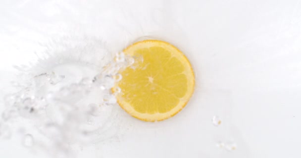 Auf weißem Hintergrund fällt ein Spritzer Wasser in Zeitlupe auf eine Zitronenscheibe — Stockvideo