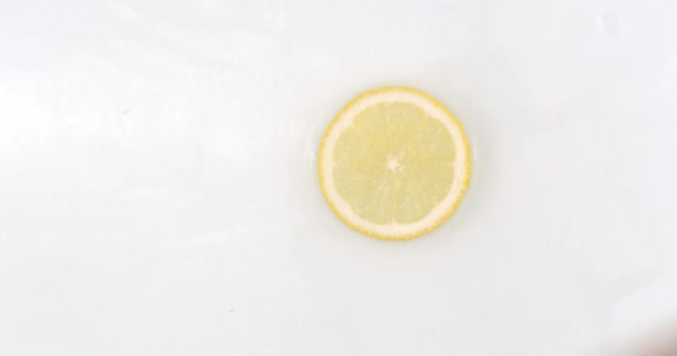 On a white background, a splash of water falls on a slice of lemon in slow motion — Stock Video