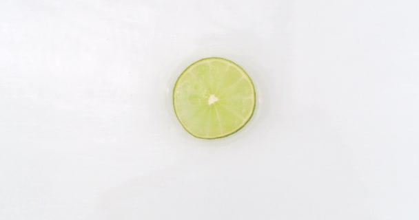 On a white background cut into slices of lime sprinkled with water spray. Juicy fresh lime in slow motion — Stock Video