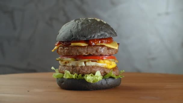 Hamburguesa o hamburguesa con pan negro sobre un fondo borroso de hojas . — Vídeos de Stock