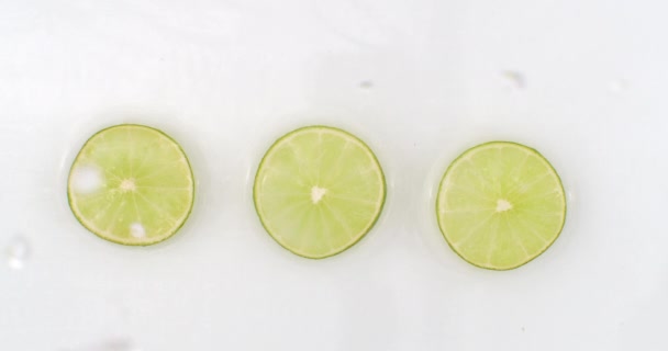 Gotas de agua caen sobre tres pedazos de cal sobre un fondo blanco — Vídeo de stock