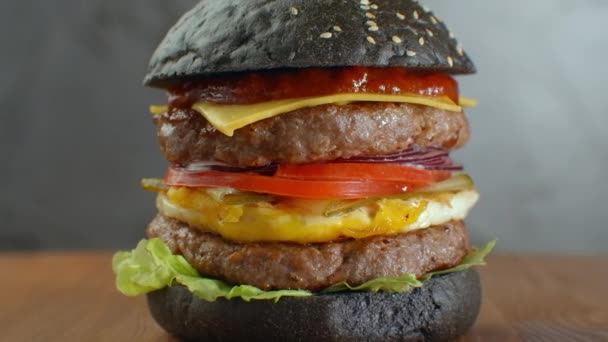 Hamburguesa o hamburguesa con pan negro sobre un fondo borroso de hojas . — Vídeos de Stock