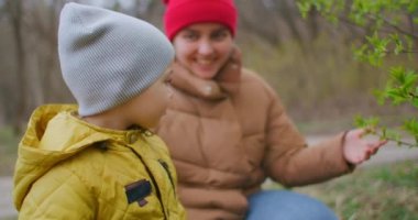 2 yaşındaki bir çocuk ormandaki ağaçlardaki yapraklara bakıyor. Bir çocuk ormanda annesiyle birlikte dünyayı öğreniyor. Mutlu gülümseyen çocuk