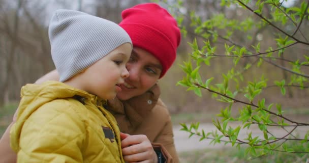 Két éves fiú nézi a leveleket az erdőben. Egy fiú tanulmányozza a világot az anyjával az erdőben. Boldog mosolygó gyermek. — Stock videók