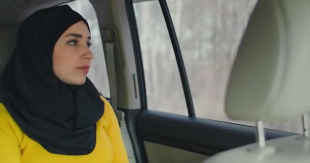 Een serieuze, attente Arabische vrouw in een auto op de passagiersstoel. Rijdt in de auto en kijkt uit het raam. Een moslimvrouw in een hijab rijdt achterin een auto — Stockvideo