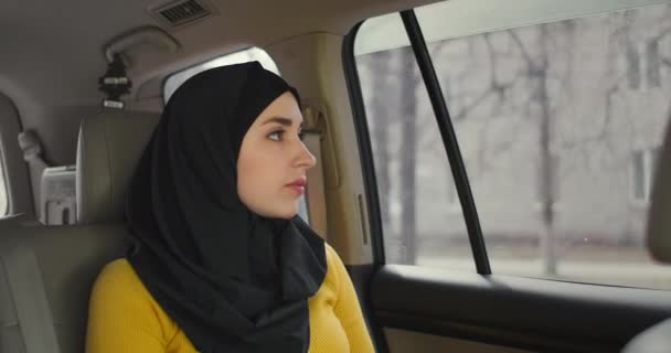 Een serieuze, attente Arabische vrouw in een auto op de passagiersstoel. Rijdt in de auto en kijkt uit het raam. Een moslimvrouw in een hijab rijdt achterin een auto — Stockvideo