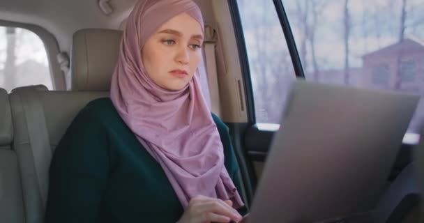 Affärskvinna i Hijab använder laptop sittandes i baksätet på bilen. Modern arabisk affärskvinna med bärbar dator och ridning taxi, upptagen kvinna sitter i taxi och gå till kontoret — Stockvideo