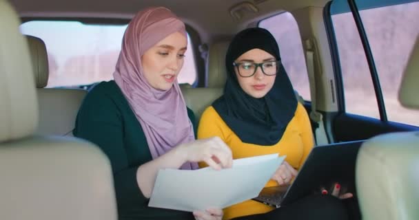 Молодые арабские бизнесвумен с двумя ноутбуками на задних сидениях автомобиля. Командная работа над переездом 2 Современная мусульманская деловая женщина в автомобиле. Два саудовских бизнесмена-коллеги, работающие с ноутбуком в автомобиле — стоковое видео