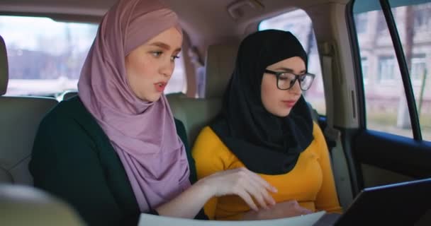 Perempuan pengusaha Arab muda dengan dua laptop di kursi belakang mobil. Kerja sama bergerak 2 Wanita bisnis Muslim modern di mobil. Dua Koleganya pengusaha Saudi bekerja sama dengan Laptop In Car — Stok Video