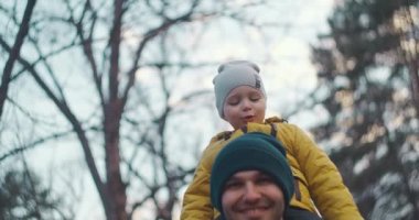 Babam çocuğu omuzlarına aldı ve banliyö parkında taşıdı. Baba oğlunu omuzlarında taşır ve parkta yürür. Sarı ceketli bir oğul ve baba ormanda yürüyor..