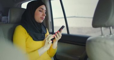 Arabadaki yolcu koltuğundaki tesettürlü güzel müslüman kadın ciddi bir ifadeyle cep telefonuna yazı yazıyor. İnternet bankası. Akıllı telefonda çalışan iş kadını. Kalabalık kaynaklı bir taksinin arka koltuğunda.