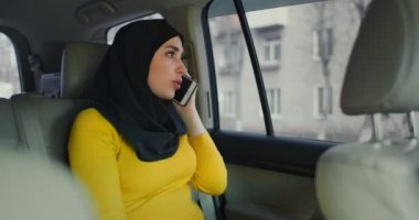 Takside arka koltukta oturan ve cep telefonuyla konuşan tesettürlü genç, çekici Müslüman kadın. Genç, modern bir Arap kadın yeni bir cep telefonuyla konuşuyor. Modern Arap kadını.