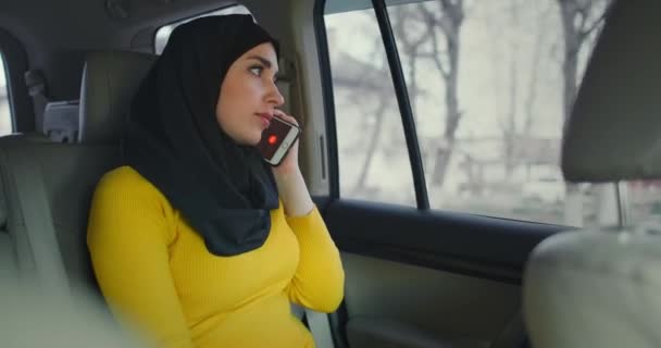 Молодая привлекательная мусульманка в хиджабе сидит на заднем сиденье в такси и разговаривает по мобильному телефону. Молодая арабская женщина разговаривает по новому сотовому телефону. Современная арабка . — стоковое видео