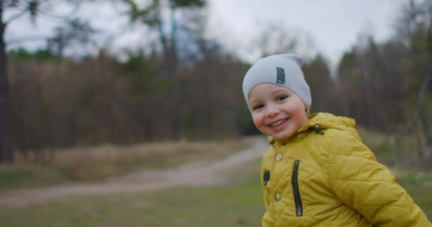 Šťastné dítě běží ke kameře venku v parku zpomalit. Malý chlapec běží lesem. Šťastný rozesmátý chlapec běží a emocionálně si hraje v lese — Stock video