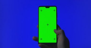 Eldeki telefon mavi arkaplanda izole edilmiş. Telefon ekranı mavi krom anahtar, arka plan krom anahtar yeşil ekran. Mobil reklamlar, uygulama tanıtımı